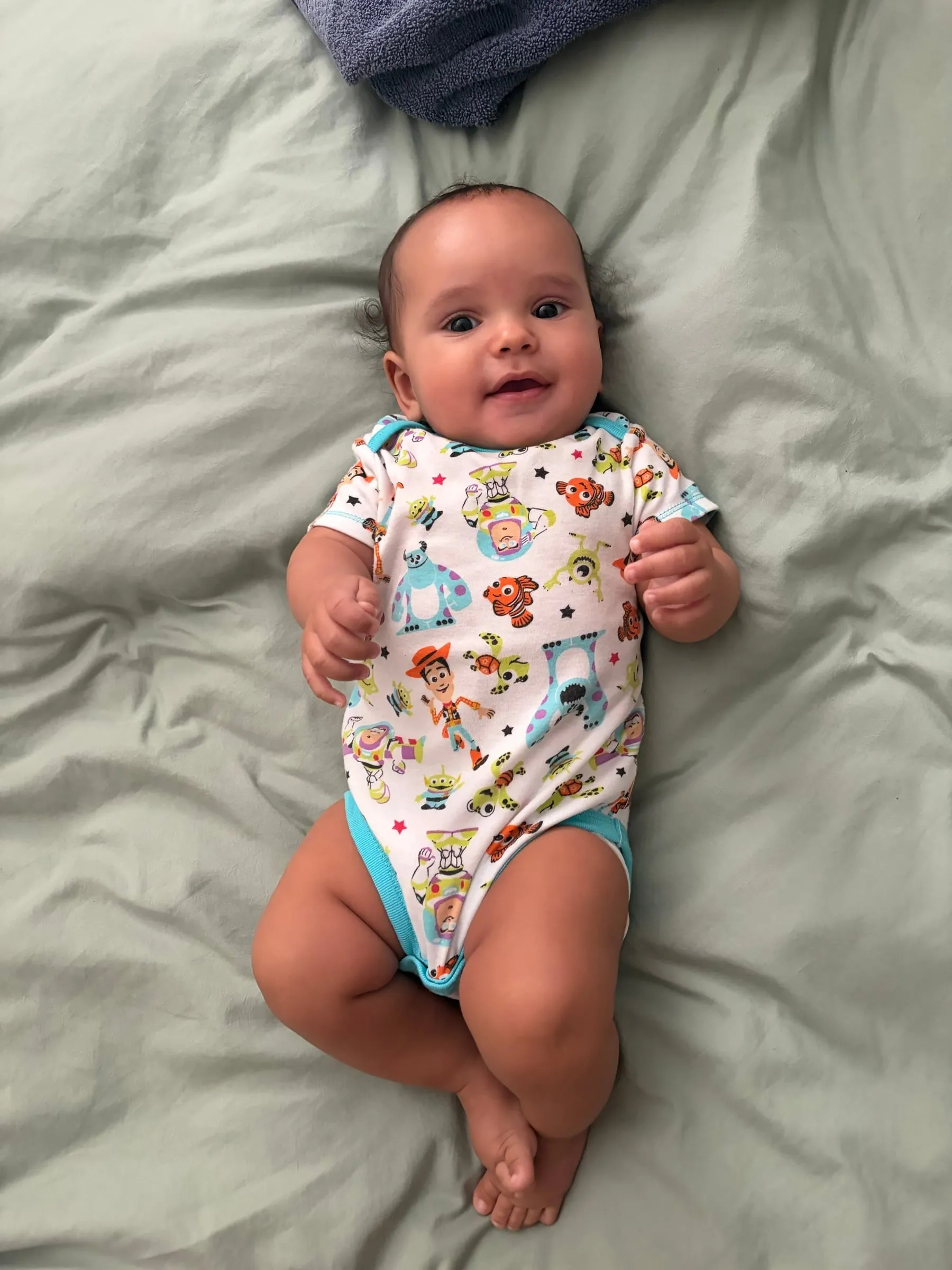 Noah smiling on a sage bed in a Toy Story onesie