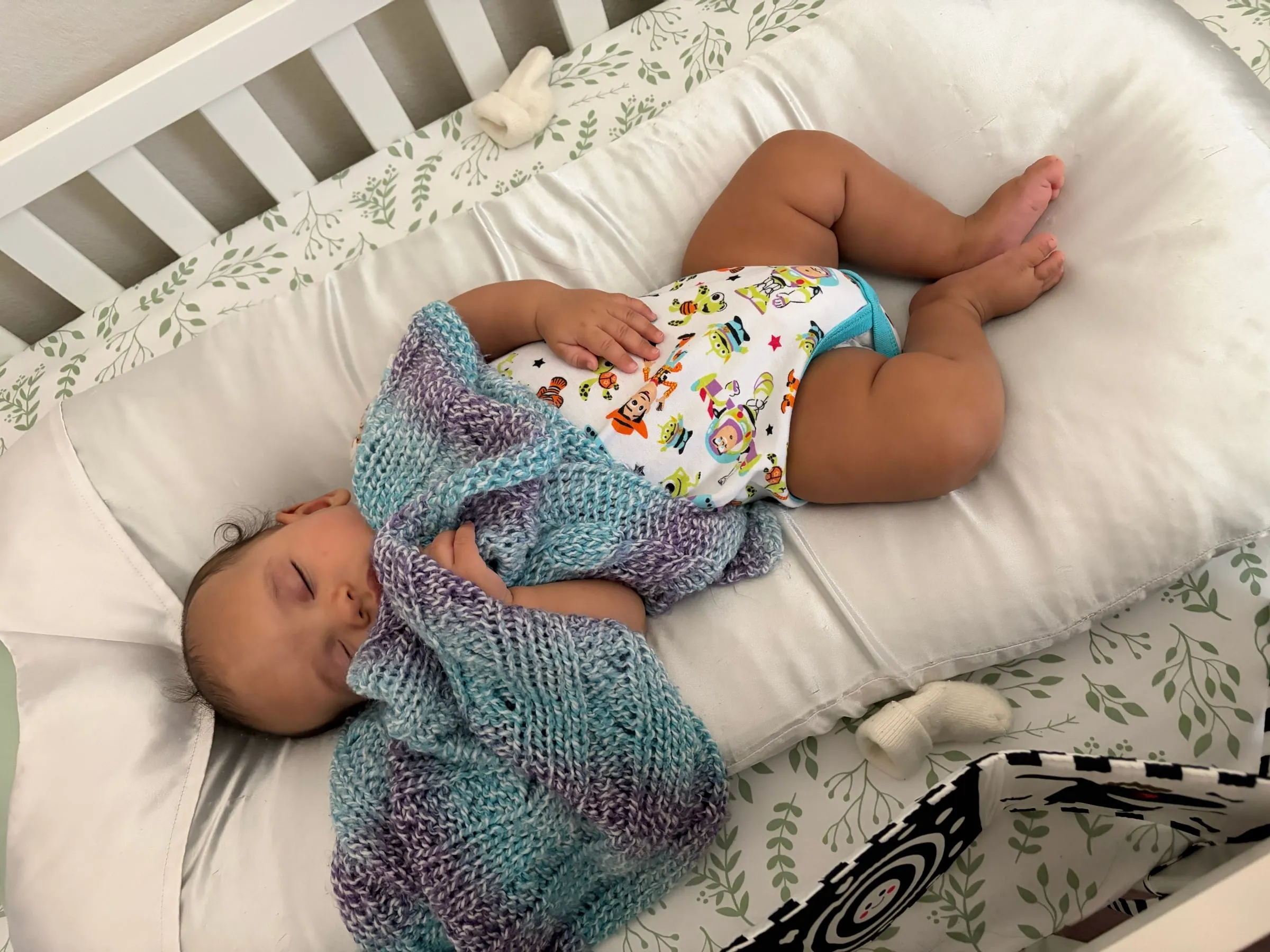 Noah asleep in his crib with a blue and purple blanket