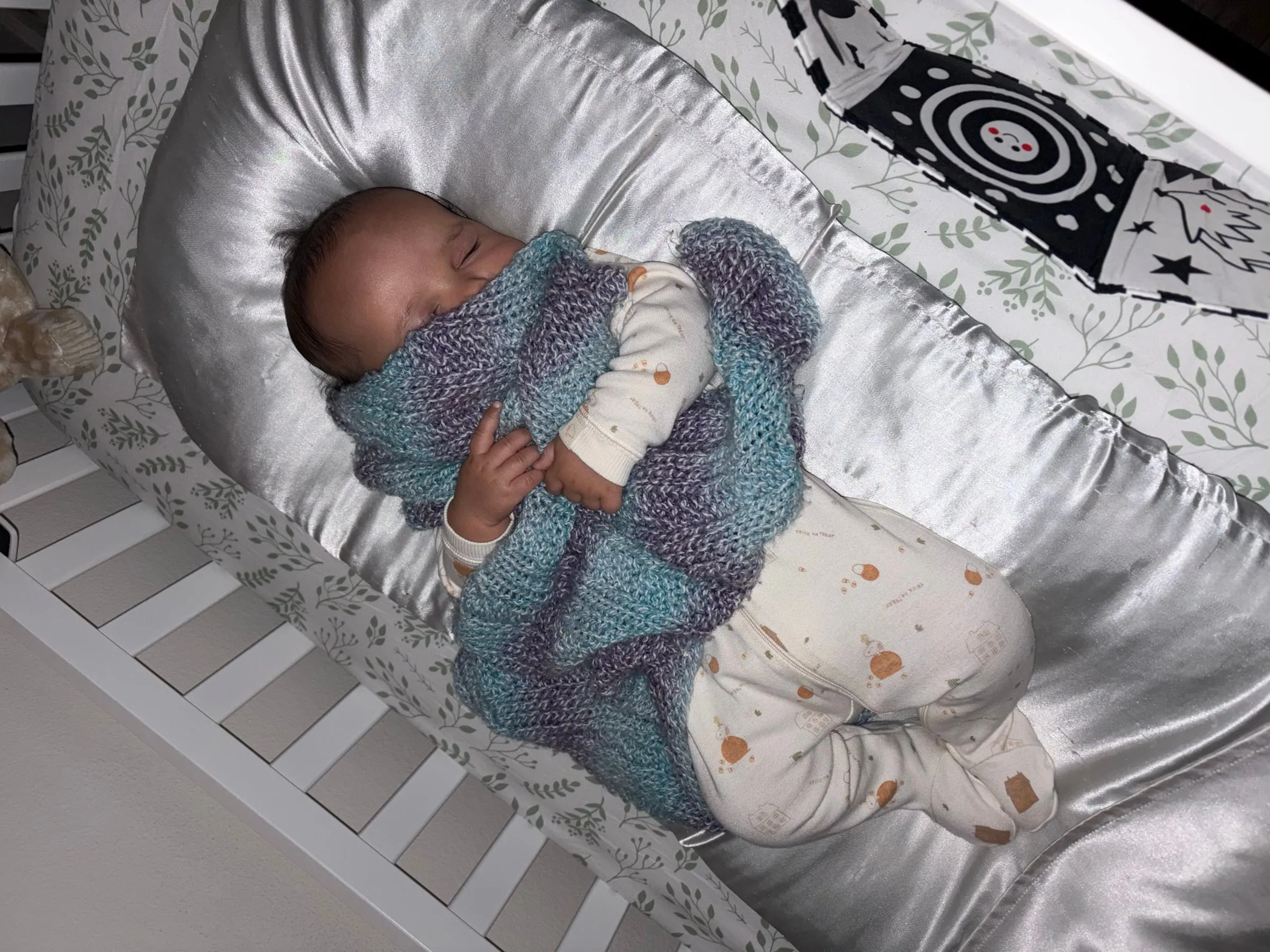 Noah asleep in his crib wrapped in a blue and purple blanket