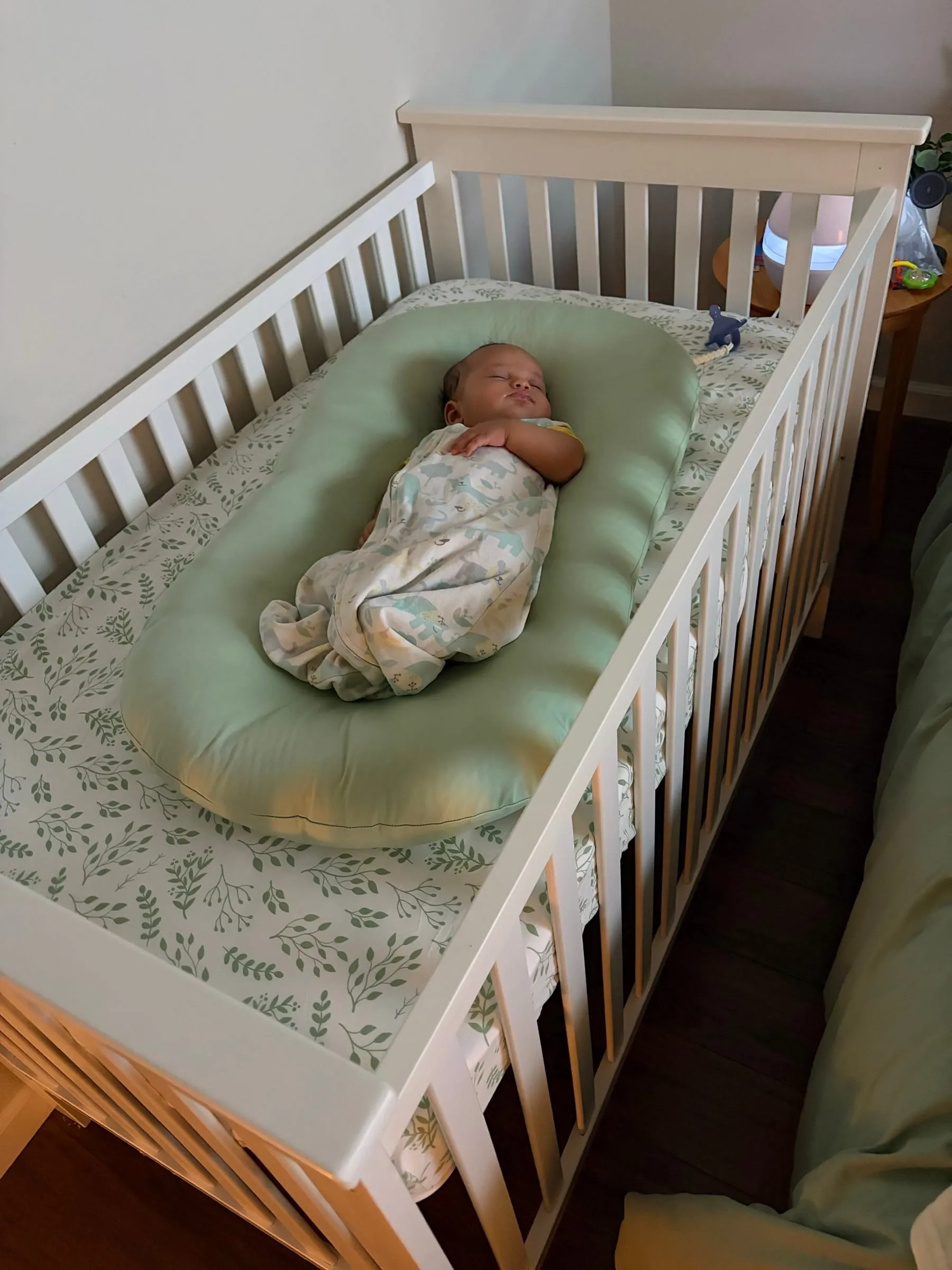 Noah swaddled and awake in his crib on a sage pillow