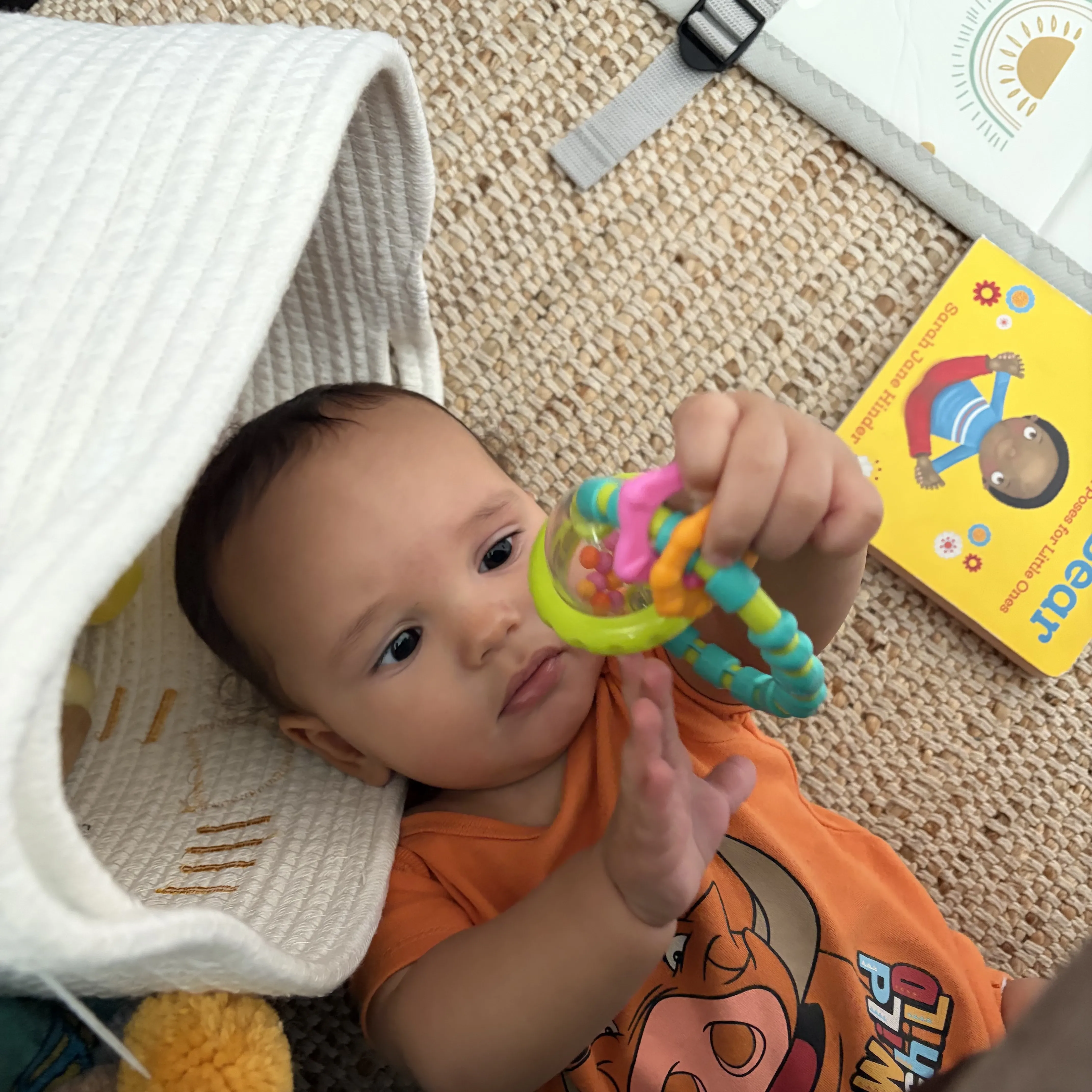 Noah lying on a rug chewing on a colorful rattle teether toy
